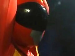 Sexy Super Hero in orange latex is strung up and tortured b